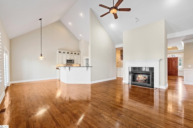 unfurnished living room with ceiling fan, high vaulted ceiling, a tile fireplace, wood finished floors, and visible vents