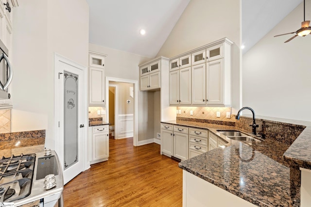 kitchen with light wood-style flooring, glass insert cabinets, a sink, dark stone counters, and a peninsula