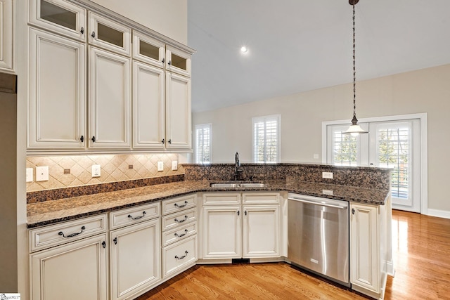 kitchen featuring a peninsula, a sink, stainless steel dishwasher, light wood finished floors, and decorative light fixtures