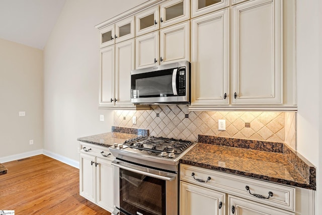 kitchen featuring light wood finished floors, tasteful backsplash, baseboards, dark stone countertops, and stainless steel appliances