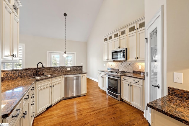 kitchen with light wood finished floors, tasteful backsplash, lofted ceiling, stainless steel appliances, and a sink