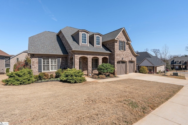 french country home with a garage, concrete driveway, brick siding, and a shingled roof