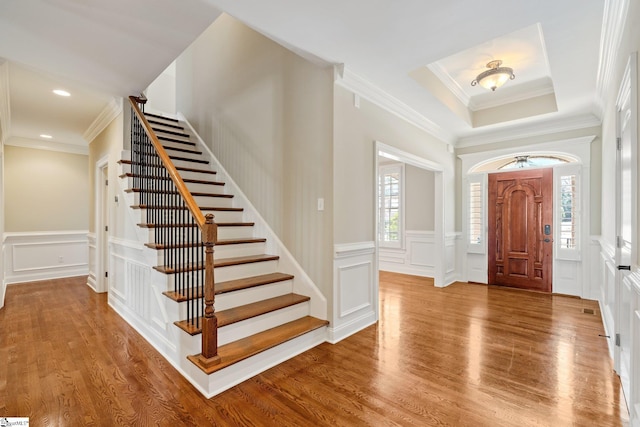 entrance foyer with stairs, ornamental molding, wood finished floors, and a decorative wall