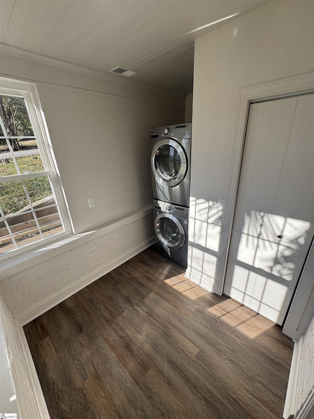 clothes washing area with laundry area, stacked washer / dryer, dark wood finished floors, and visible vents