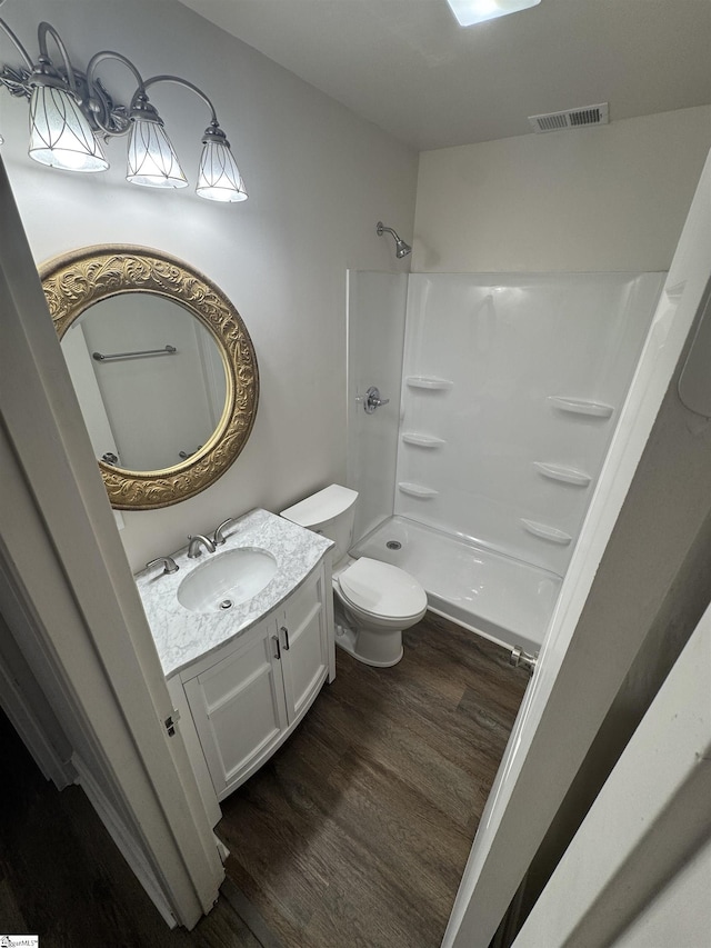 bathroom featuring visible vents, a shower, toilet, wood finished floors, and vanity