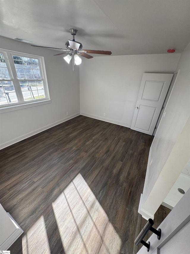 empty room with ceiling fan, dark wood-type flooring, visible vents, and baseboards