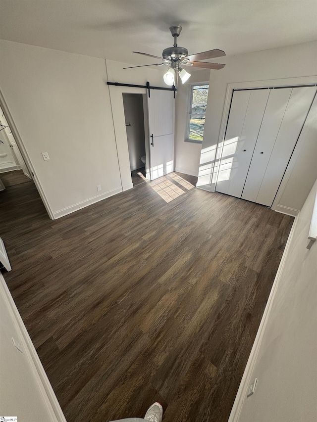 unfurnished bedroom with a ceiling fan, a closet, dark wood finished floors, and a barn door
