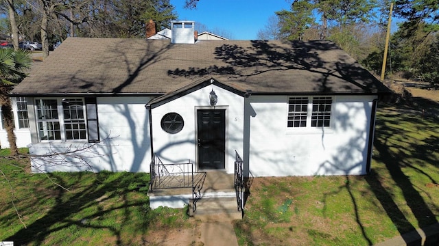 view of front of property with a shingled roof, a chimney, and a front yard