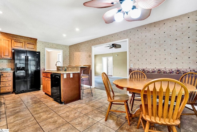 kitchen with a ceiling fan, a kitchen island with sink, a sink, black appliances, and wallpapered walls