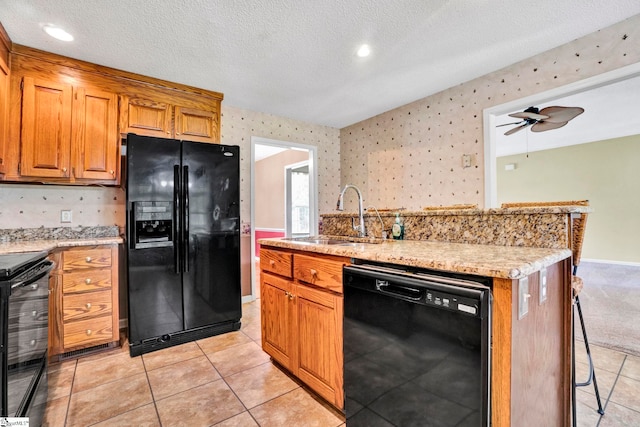 kitchen featuring black appliances, wallpapered walls, a kitchen breakfast bar, and a sink