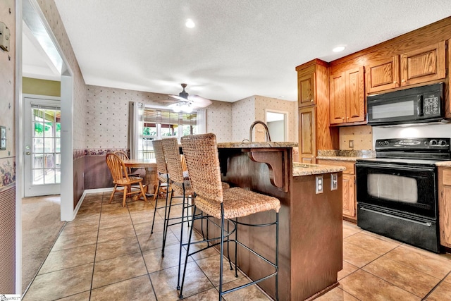 kitchen with black appliances, wallpapered walls, a breakfast bar area, and a textured ceiling