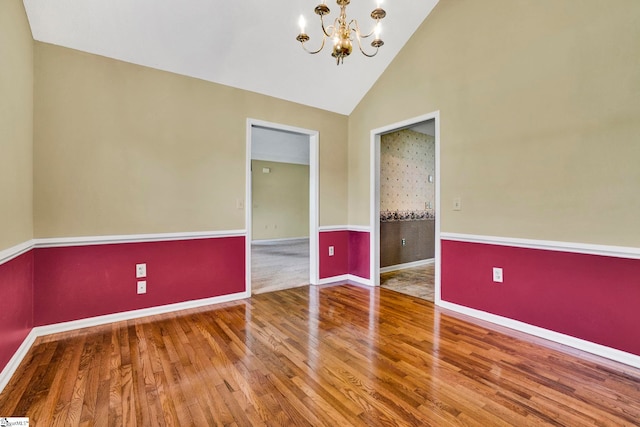 empty room featuring high vaulted ceiling, a notable chandelier, baseboards, and wood finished floors