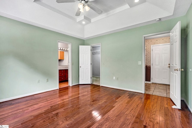 unfurnished bedroom featuring baseboards, connected bathroom, ceiling fan, wood finished floors, and a tray ceiling