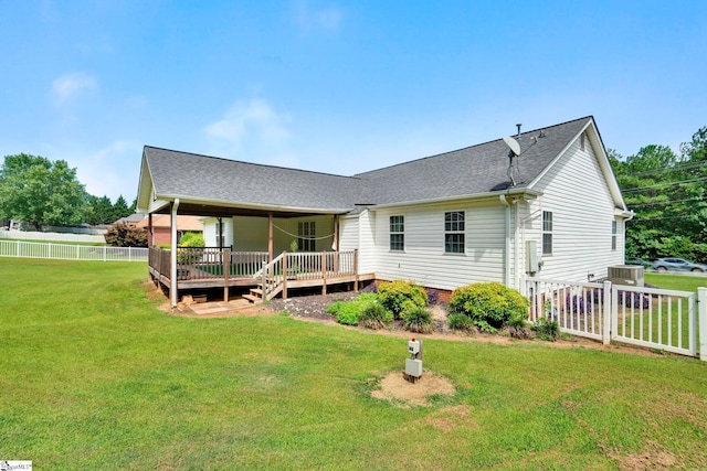 rear view of property featuring a shingled roof, a lawn, a deck, and fence