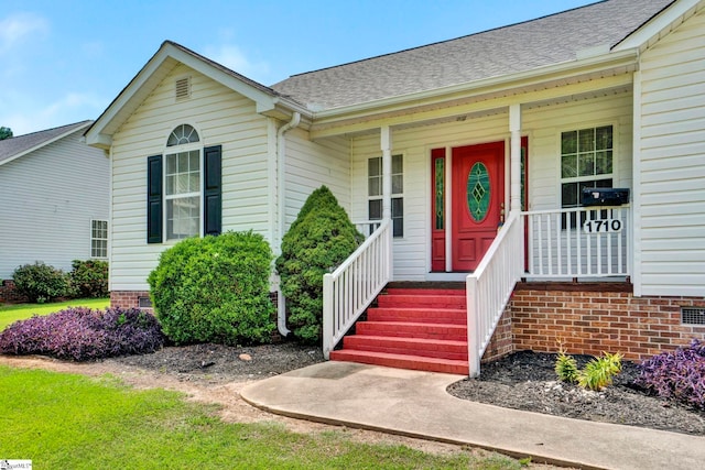 entrance to property with covered porch, a shingled roof, and crawl space