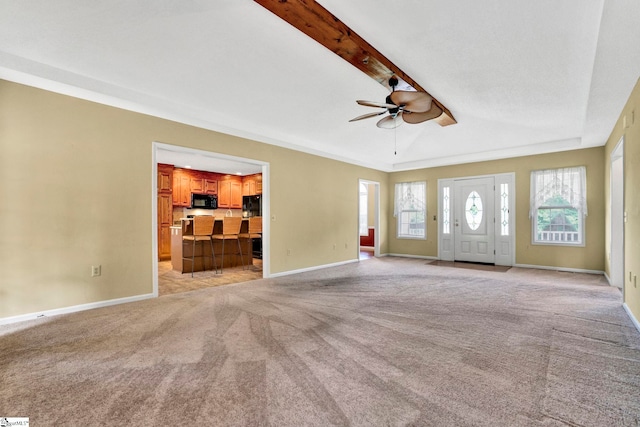 unfurnished living room featuring a ceiling fan, light colored carpet, beamed ceiling, and baseboards