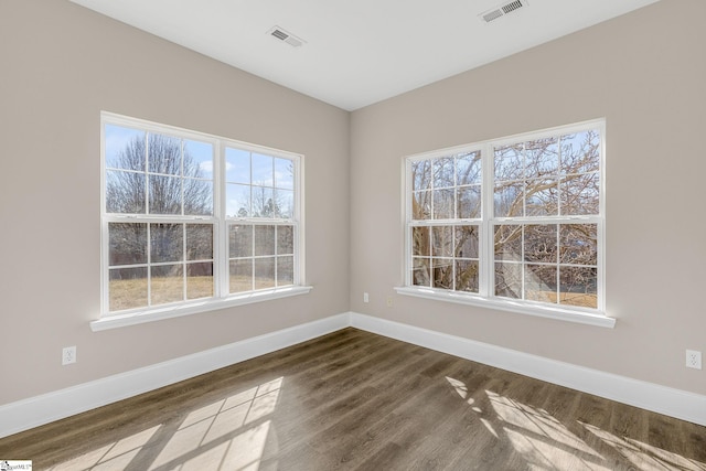 spare room with dark wood-type flooring, visible vents, and baseboards