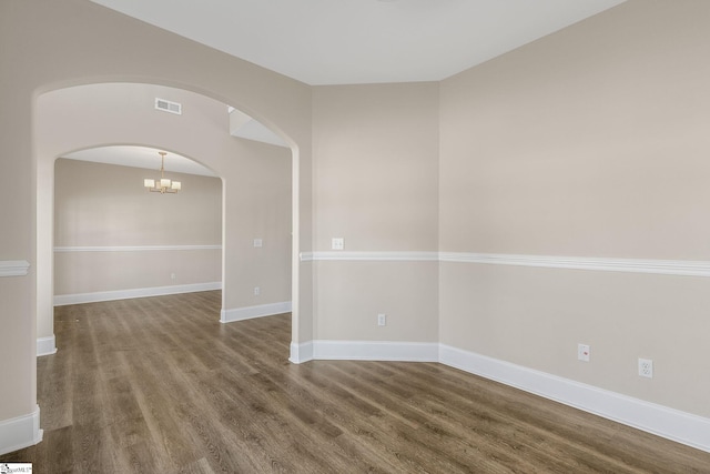 unfurnished room featuring arched walkways, a notable chandelier, visible vents, wood finished floors, and baseboards