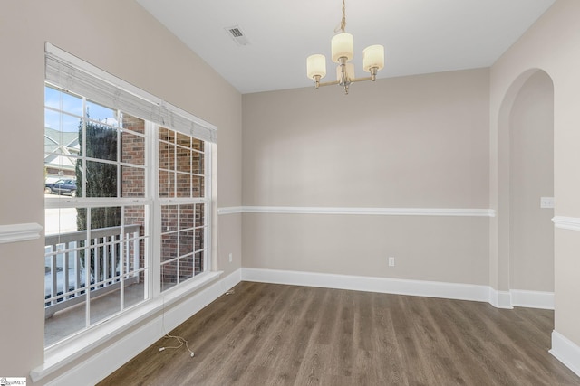 empty room featuring arched walkways, a notable chandelier, visible vents, wood finished floors, and baseboards