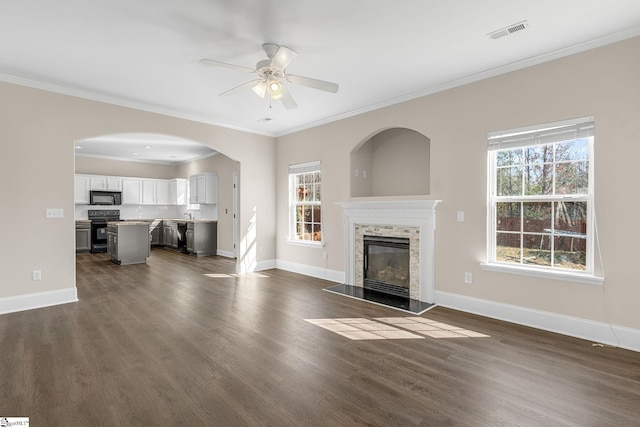 unfurnished living room with dark wood-style flooring, visible vents, ornamental molding, a glass covered fireplace, and baseboards