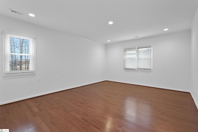 spare room with baseboards, hardwood / wood-style floors, visible vents, and a healthy amount of sunlight