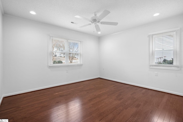 empty room with a textured ceiling, dark wood finished floors, visible vents, and a healthy amount of sunlight