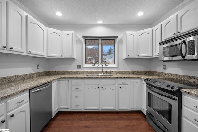 kitchen featuring dark wood-style flooring, stainless steel appliances, a textured ceiling, white cabinetry, and a sink