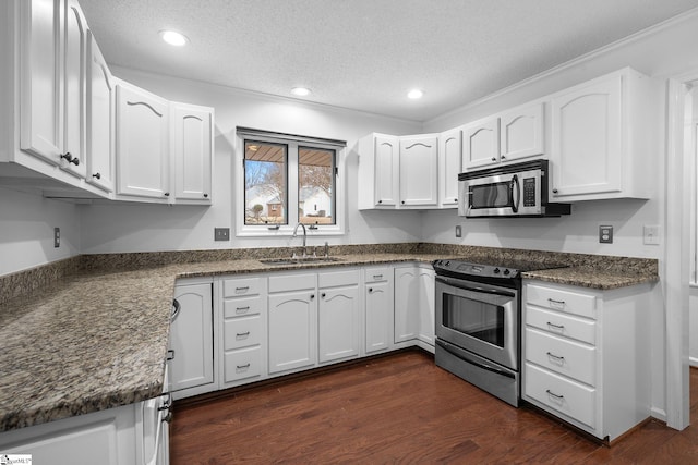 kitchen featuring appliances with stainless steel finishes, white cabinetry, a sink, and dark wood-type flooring