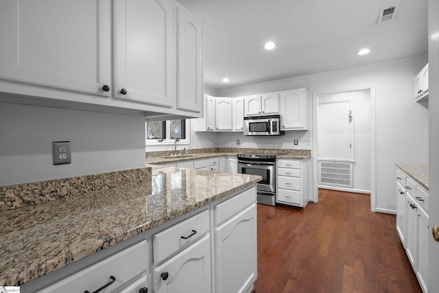 kitchen with light stone counters, a sink, white cabinets, appliances with stainless steel finishes, and dark wood finished floors