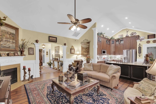 living room featuring lofted ceiling, a fireplace with flush hearth, visible vents, wainscoting, and dark wood finished floors