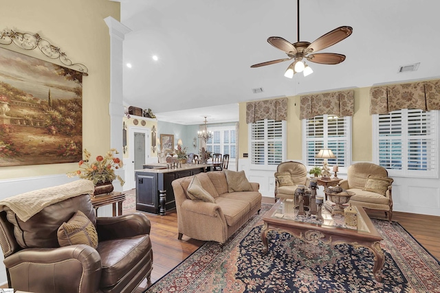 living area featuring ceiling fan with notable chandelier, visible vents, a decorative wall, and wood finished floors