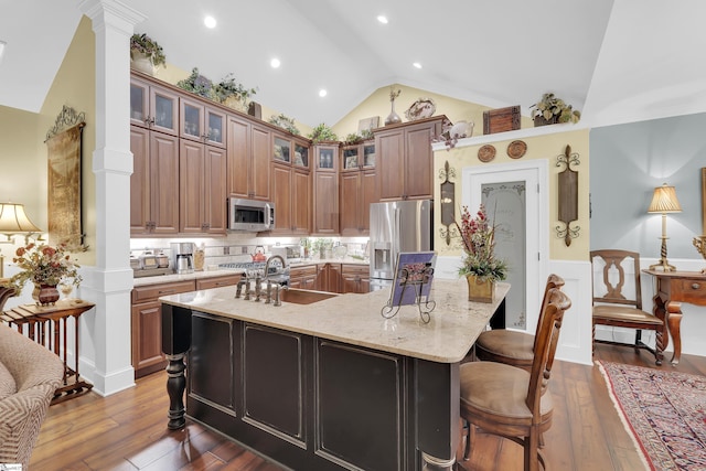 kitchen with lofted ceiling, a wainscoted wall, stainless steel appliances, a sink, and ornate columns