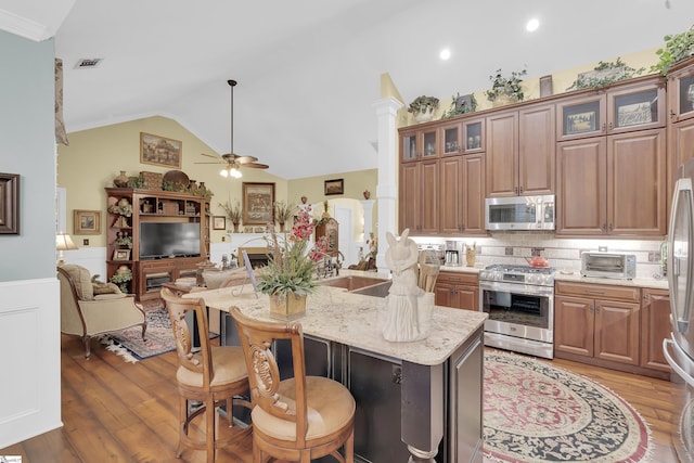 kitchen featuring stainless steel appliances, lofted ceiling, open floor plan, a sink, and light stone countertops