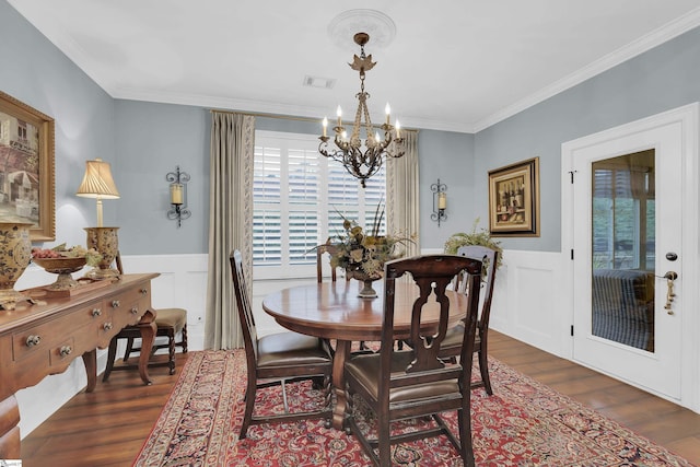 dining space with a wainscoted wall, crown molding, dark wood finished floors, a notable chandelier, and visible vents