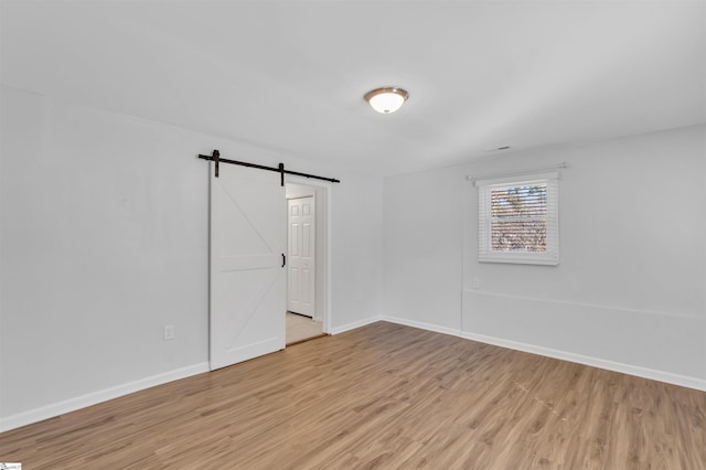 spare room featuring baseboards, light wood finished floors, and a barn door