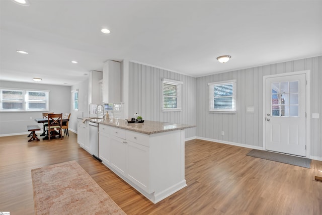 kitchen featuring white cabinetry, light wood-style flooring, stainless steel dishwasher, and light stone countertops