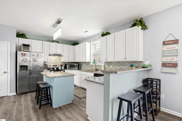 kitchen featuring white cabinets, a breakfast bar, wood finished floors, stainless steel appliances, and under cabinet range hood