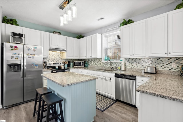 kitchen featuring under cabinet range hood, stainless steel appliances, a sink, white cabinets, and light wood-type flooring