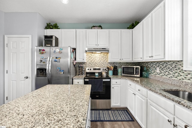 kitchen with tasteful backsplash, appliances with stainless steel finishes, white cabinetry, and under cabinet range hood