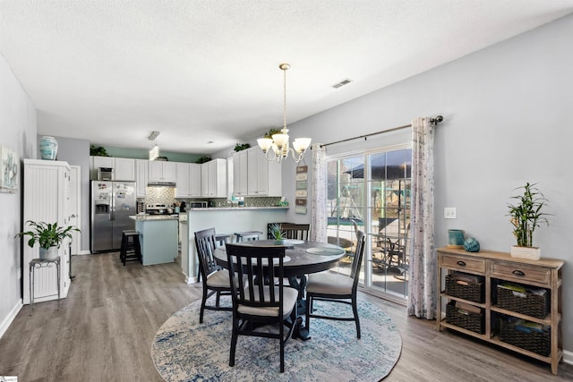 dining room featuring a textured ceiling, visible vents, baseboards, light wood-type flooring, and an inviting chandelier