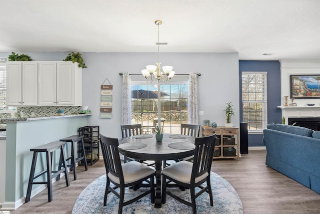 dining room featuring baseboards, a fireplace, light wood-style flooring, and a notable chandelier