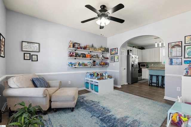 interior space featuring arched walkways, ceiling fan, dark wood-style floors, and baseboards