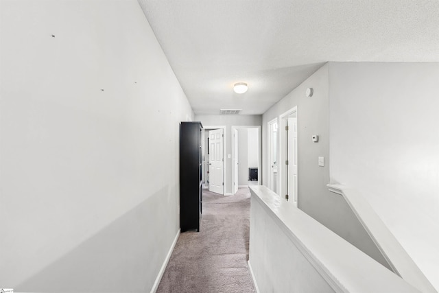 corridor with visible vents, light carpet, a textured ceiling, and baseboards