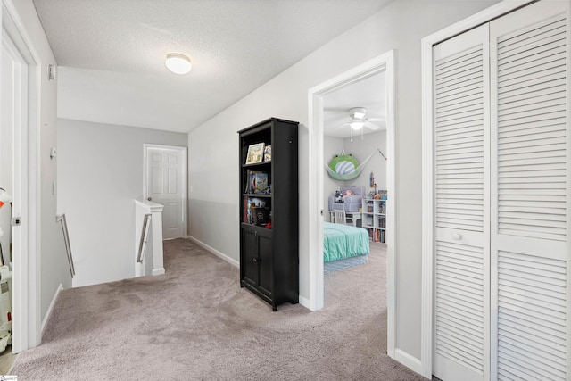 hallway featuring a textured ceiling, carpet floors, an upstairs landing, and baseboards