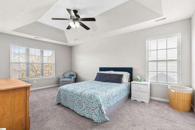 bedroom with carpet floors, a tray ceiling, visible vents, and baseboards