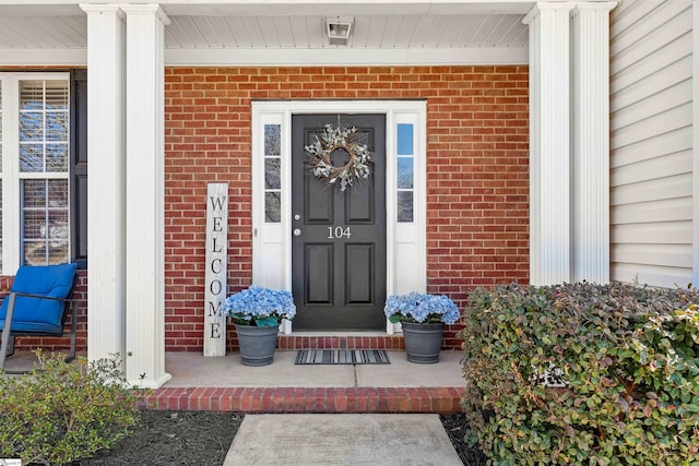 doorway to property with a porch and brick siding