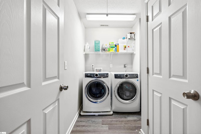 clothes washing area with laundry area, visible vents, wood finished floors, independent washer and dryer, and a textured ceiling