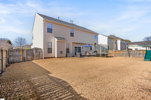 back of house with a trampoline, a playground, and a fenced backyard