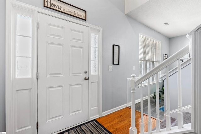 entrance foyer featuring light wood finished floors, visible vents, stairway, and baseboards