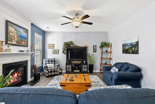 living room featuring a ceiling fan, baseboards, dark wood-style flooring, and a glass covered fireplace